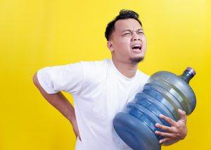 A man struggling to carry a heavy water jug for a water cooler. Workplace hazard concept.