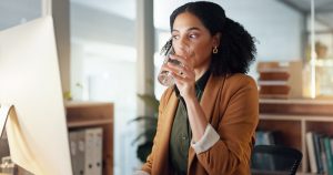 Woman at desk with computer, drinking water. Hydration at work concept.